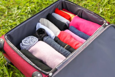 Yeşil çimlerin üzerinde farklı giysiler katlanmış bir şekilde bavulu aç. Seyahat paketinde kolay ve küçük alan tasarrufu için dikey depolama