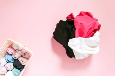 Ev gardırobunda renkli kıyafetler dikey depolanmış. Yumuşak pembe arka planda tekstil kutusunda giysi parçaları