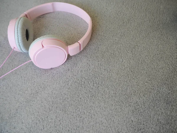 Large pink headphones with a cord lie on a gray structural background