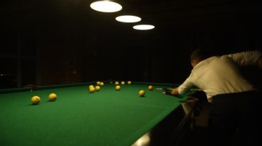 Beyaz gömlekli genç adam bilardo oynuyor..