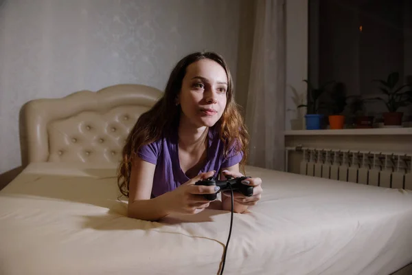 Ragazza gamer gioca con un gamepad mentre guarda lo schermo di fronte a lei . — Foto Stock
