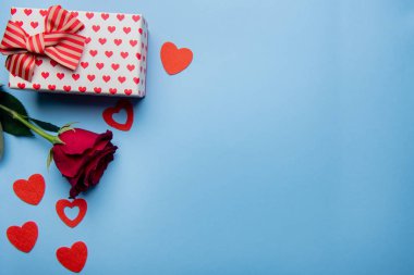 Kırmızı kalpli hediye kutusu ve mavi arka planda gül.