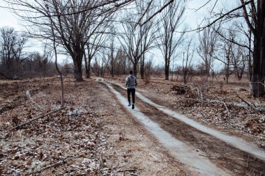Adam dışarıda koşuyor, güneşli bir sonbahar sabahında antrenman yapıyor. Genç atletik adam soğuk bir sonbahar sabahı parkta koşuyor.