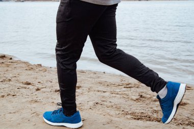 Spor giyimli genç adam plajda koşuyor. Koşucu soğuk havada sahilde antrenman yapıyor..