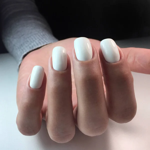 Woman's hands with white nails on the dark background. Nail varnishing in white color. Manicure beauty salon concept. Empty place for text or logo.