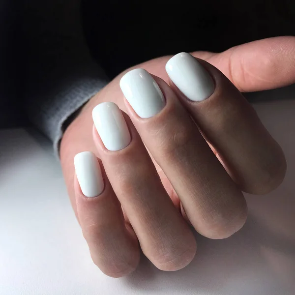 Woman\'s hands with white nails on the dark background. Nail varnishing in white color. Manicure beauty salon concept. Empty place for text or logo.