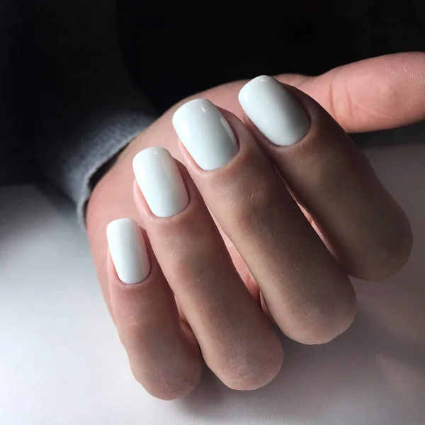 Woman's hands with white nails on the dark background. Nail varnishing in white color. Manicure beauty salon concept. Empty place for text or logo.