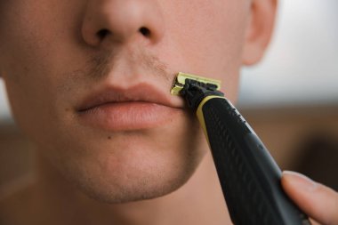 Genç adam bıyığını budayıcı ile kesiyor, yakın plan.