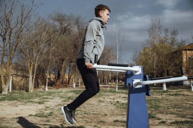 Açık hava spor salonundaki düz olmayan barlarda şınav çeken genç adam. Egzersiz yaşam tarzı konsepti.