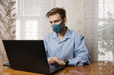 Adam dizüstü bilgisayarla tıbbi maske takıyor. Diğer insanlarla temastan kaçının. Evde kal. Evden çalışıyorum. Çevrimiçi.