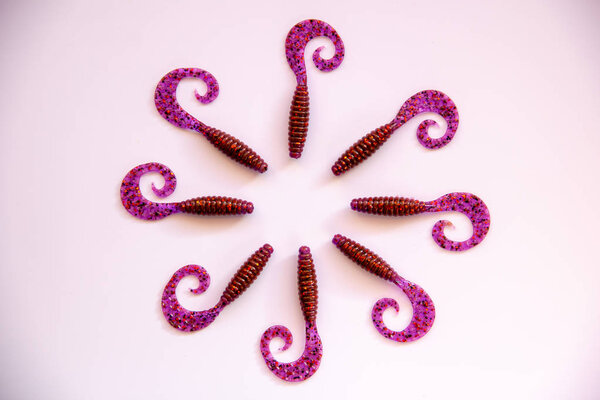 Группа изолированных силиконовых приманки лежат вокруг на белом фоне. Фиолетовые пластиковые мягкие приманки для прядильной рыбалки. Плоский лежал
.