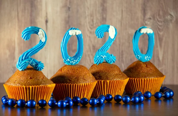 Cupcakes decorated with sweet blue numbers, beads on a wooden background. New Year 2020 concept. Copy space for your text.