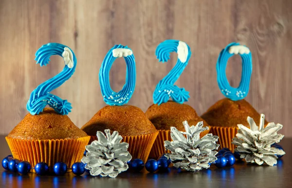 Cupcakes decorated with sweet blue numbers, beads, cones on a wooden background. New Year 2020 concept. Copy space for your text.