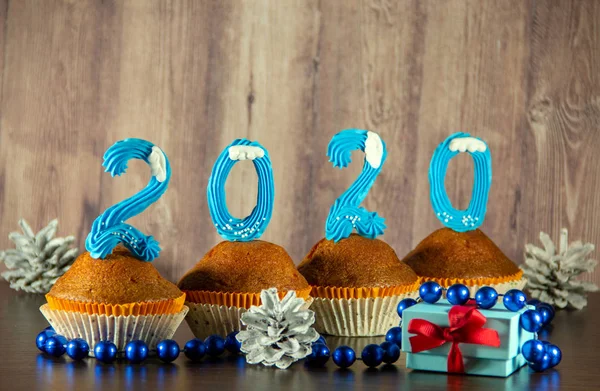 Cupcakes decorated with sweet blue numbers, gift box, beads, cones on a wooden background. New Year 2020 concept. Copy space for your text.