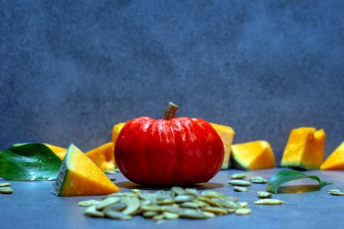 Olgun küçük balkabağı, balkabağı parçaları, yeşil yapraklar, kabak tohumları. Yatay görünüm.