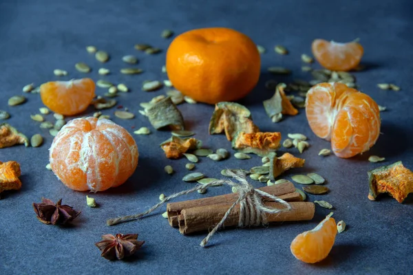 Ripe mandarin peeled mandarin, slices of mandarin, star anise, cinnamon sticks decorated with twine, seeds and pieces of dried fruit on a gray background.