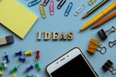 Kağıt ataç, kalem, kalem, kağıt, klasör, silgi, düğme, cep telefonu etrafında tahta harflerden oluşan fikir. Yaratıcı bir kavram. Üst manzara, düz uzanma. 