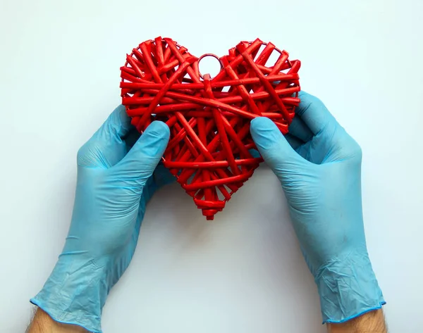 Hands in blue medical gloves are holding a red heart made of twigs. Protection against pollution, viruses, flu and coronavirus. Healthcare concept. Flat lay, copy space.