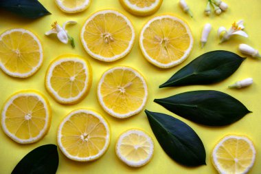 Sarı limon dilimleri, sarı arka planda limon ağacı yaprakları ve çiçekleri olan yaratıcı bir düzen. Minimum yaz konsepti. Düz yatıyordu. Boşluğu kopyala, kağıt kart.