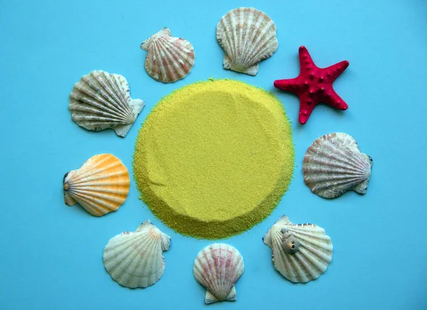 Creative pattern of seashells and red starfish, yellow sand in the shape of a circle on a bright blue background. Minimal summer concept. Flat lay. Copy space, paper card.