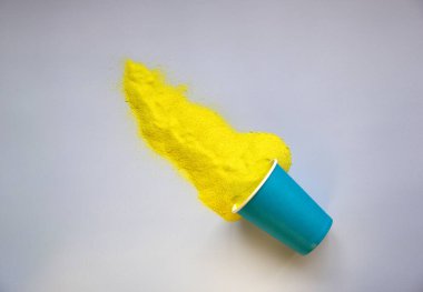 Kağıt bardaktan dağılmış sarı kum. Mavi arka planda en düşük yaz konsepti. Düz yatıyordu. Boşluğu kopyala.
