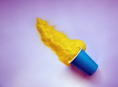 Kağıt bardaktan dağılmış sarı kum. Mavi arka planda en düşük yaz konsepti. Düz yatıyordu. Boşluğu kopyala.