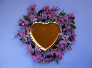 Pembe bahar ağacı çiçekleri ve mavi arka planda altın dekoratif bir kalbi olan yaratıcı bir düzen. Çiçek kompozisyonu. Asgari doğa konsepti. Düz yatıyordu. Boşluğu kopyala.