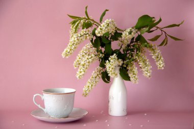 Beyaz çay fincanı ve çay tabağı, bir vazo dolusu taze kiraz, pembe arka planda taç yaprakları. Durgun hayat. Romantik bir kavram. Boşluğu kopyala.