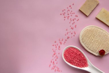 Beyaz kaşıkta doğal banyo tuzu, banyo süngeri, el yapımı sabun, pembe arka planda kuru gül. Rahatlama, vücut bakımı, organik banyo ürünleri. Spa kozmetik. Düz yatıyordu. Boşluğu kopyala.