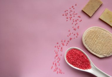 Beyaz kaşıkta doğal banyo tuzu, banyo süngeri, pembe arka planda el yapımı sabun. Rahatlama, vücut bakımı, organik banyo ürünleri. Spa kozmetik. Düz yatıyordu. Boşluğu kopyala.
