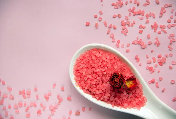 Beyaz kaşıkta doğal banyo tuzu, pembe arka planda kurumuş gül. Rahatlama, vücut bakımı, organik banyo ürünleri. Spa kozmetik. Düz yatıyordu. Boşluğu kopyala.