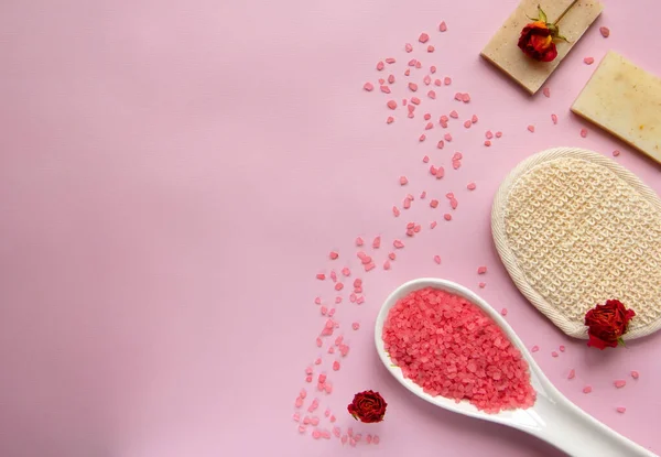 Beyaz kaşıkta doğal banyo tuzu, banyo süngeri, el yapımı sabun, pembe arka planda kuru güller. Rahatlama, vücut bakımı, organik banyo ürünleri. Spa kozmetik. Düz yatıyordu. Boşluğu kopyala.