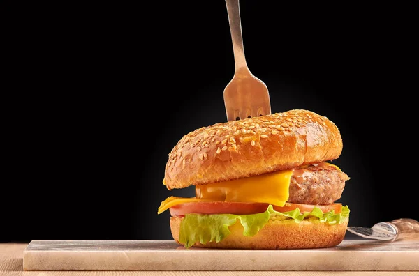Siyah arka planda çatallı el yapımı burger. Tabakta çizburger.