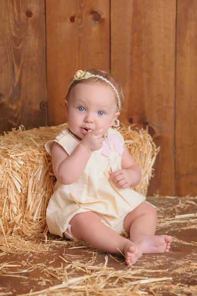 Babymeisje zit tegen een baal stro — Stockfoto