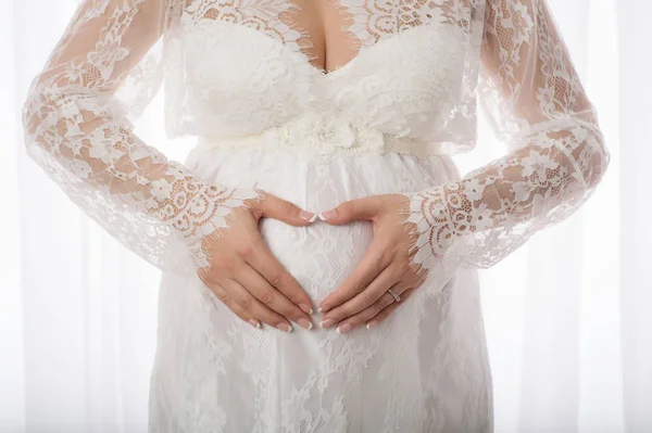 Ruce na těhotné břicho ve tvaru srdce — Stock fotografie