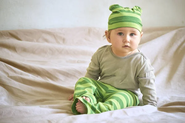 Ein Kind mit grünem Hut sitzt auf einem Bett — Stockfoto