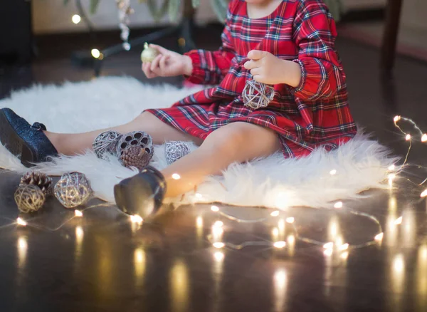 Happy little girl in a dress sitting near Christmas tree — Stock Photo, Image