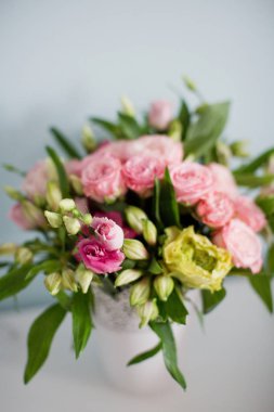 Gül desenli parlak buket, beyaz vazoda östoma ve alstromerya. Yumuşak mavi arkaplanda bir buket