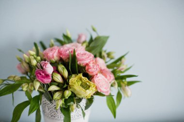 Gül desenli parlak buket, beyaz vazoda östoma ve alstromerya. Yumuşak mavi arkaplanda bir buket