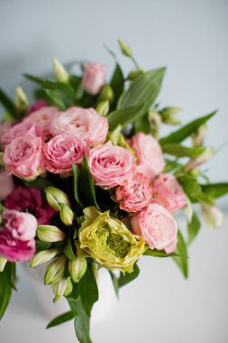 Gül desenli parlak buket, beyaz vazoda östoma ve alstromerya. Yumuşak mavi arkaplanda bir buket