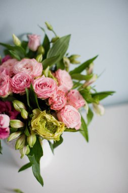 Gül desenli parlak buket, beyaz vazoda östoma ve alstromerya. Yumuşak mavi arkaplanda bir buket