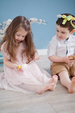 Nergis ve kayısı çiçeği dallarının yanında tatlı bir kız ve oğlan. Mavi arkaplan duvarında bahar süslemeleri