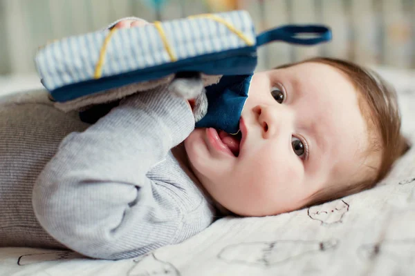 小さな赤ちゃん男の子はベッドの上に横になり ティッシュ本と遊ぶ — ストック写真