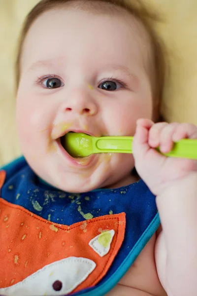 小さな男の子は緑色のスプーンから彼の最初の食べ物を食べる 可愛いです赤ちゃんで野菜のピューレを食べる — ストック写真