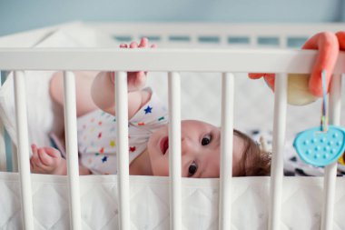 Küçük oğlan ışık odasında beşiğinde yatıyor ve oyuncaklarıyla oynuyor.