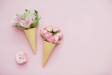 Pembe pastel arka planda pembe çiçekli dondurma külahları. Üst görünüm