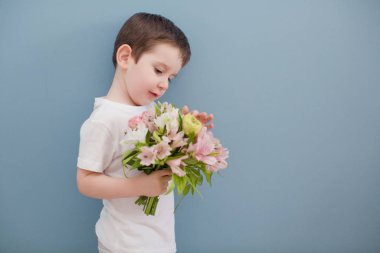 Beyaz tişörtlü küçük çocuk pembe çiçek buketi tutuyor. Mavi duvarın arkasındaki komik çocuk.