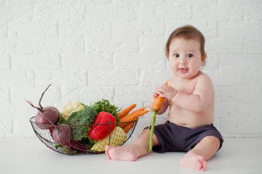 Küçük beyaz çocuk taze çiğ sebzelerin yanında oturuyor. Sağlıklı beslenme. Metal sepette taze çiğ sebzeler.