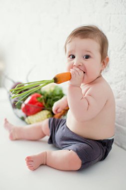 Küçük beyaz çocuk taze çiğ sebzelerin yanında oturuyor. Sağlıklı beslenme. Metal sepette taze çiğ sebzeler.