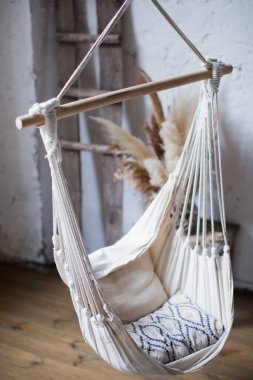 Asılı makrome salıncak beyaz duvarlı çatı katındaki iplerde sallanıyor.